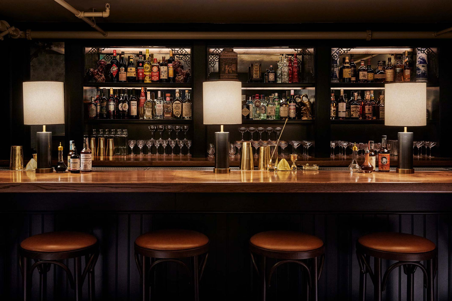 On top of the bar sits three lamps, cocktail making equipment and some bottles