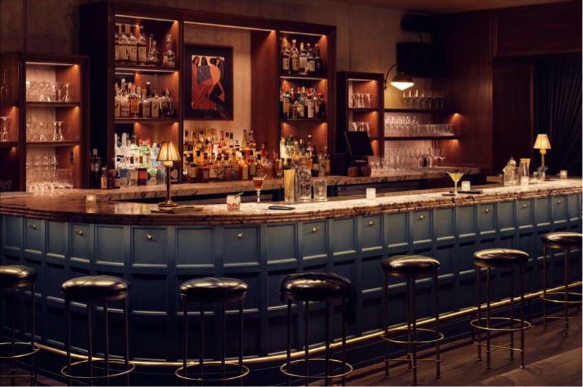 Dimly lit bar area, with several black bar stools in front of it