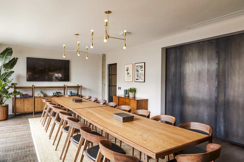 A much larger meeting room with a very long table with 20 chairs, and a TV on the far wall