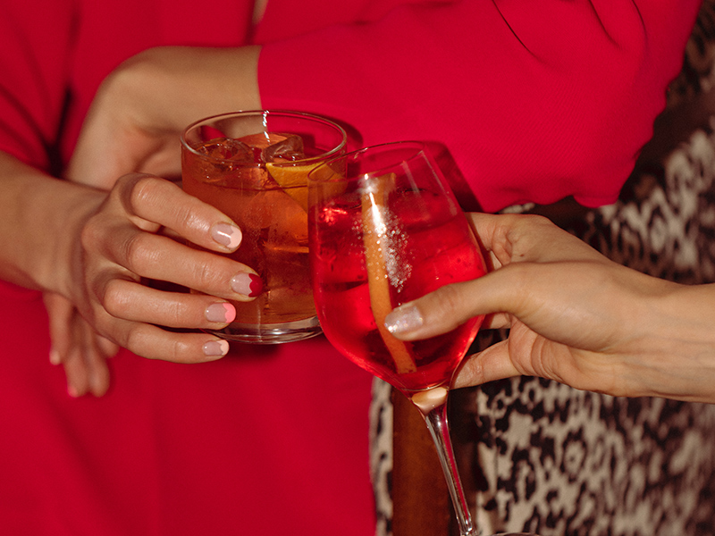 A cocktail and wine glass clink in two women's hands
