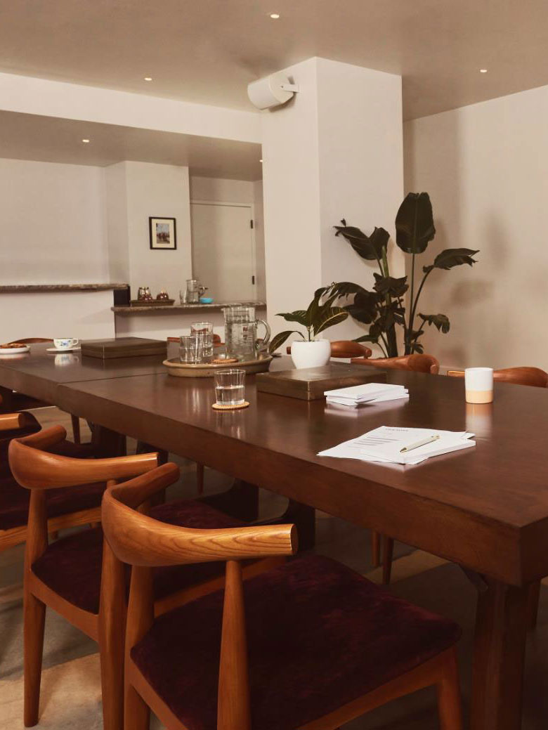 A windowless room with white walls and a long wooden table with chairs in the middle
