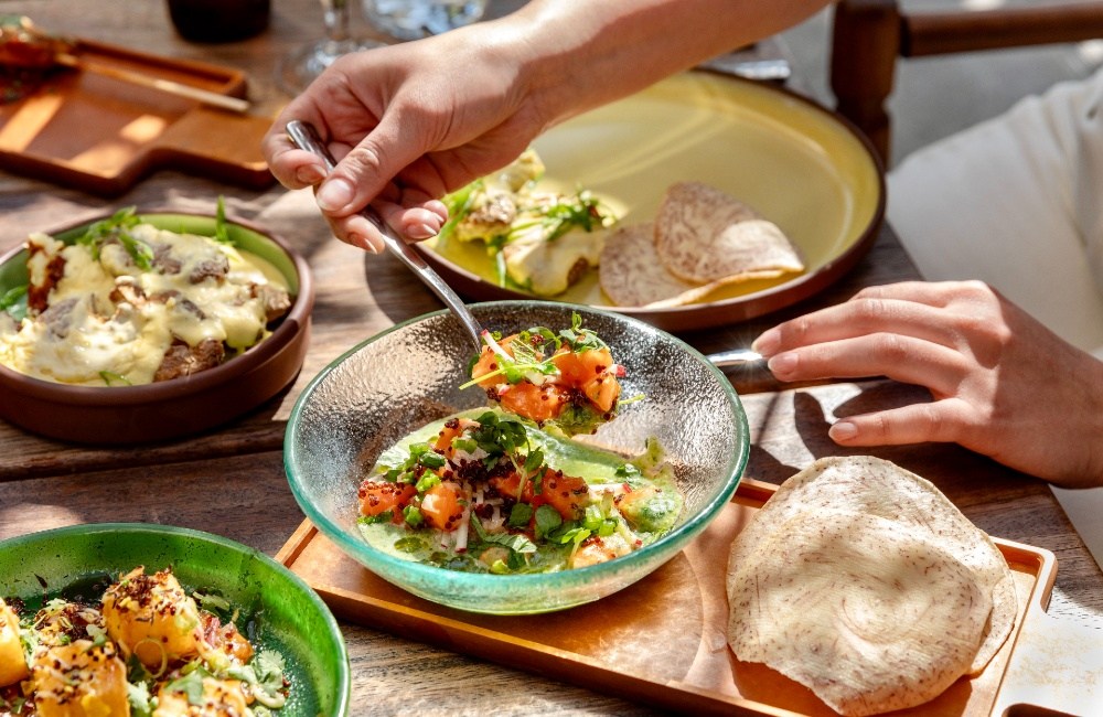 Een gerecht in levendig groen, geserveerd in een diepe, doorzichtige glazen schaal, vergezeld van andere gerechten en brood op tafel.