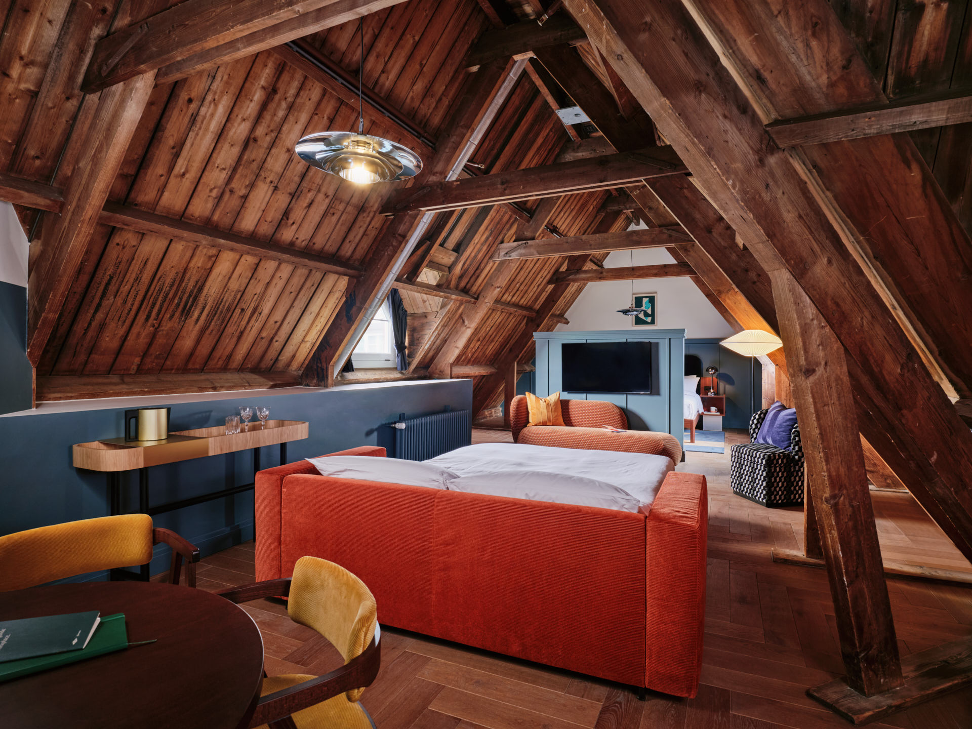 Long shot of the Studio room with bed, TV screen, bare wood ceiling and floor, and soft furnishing