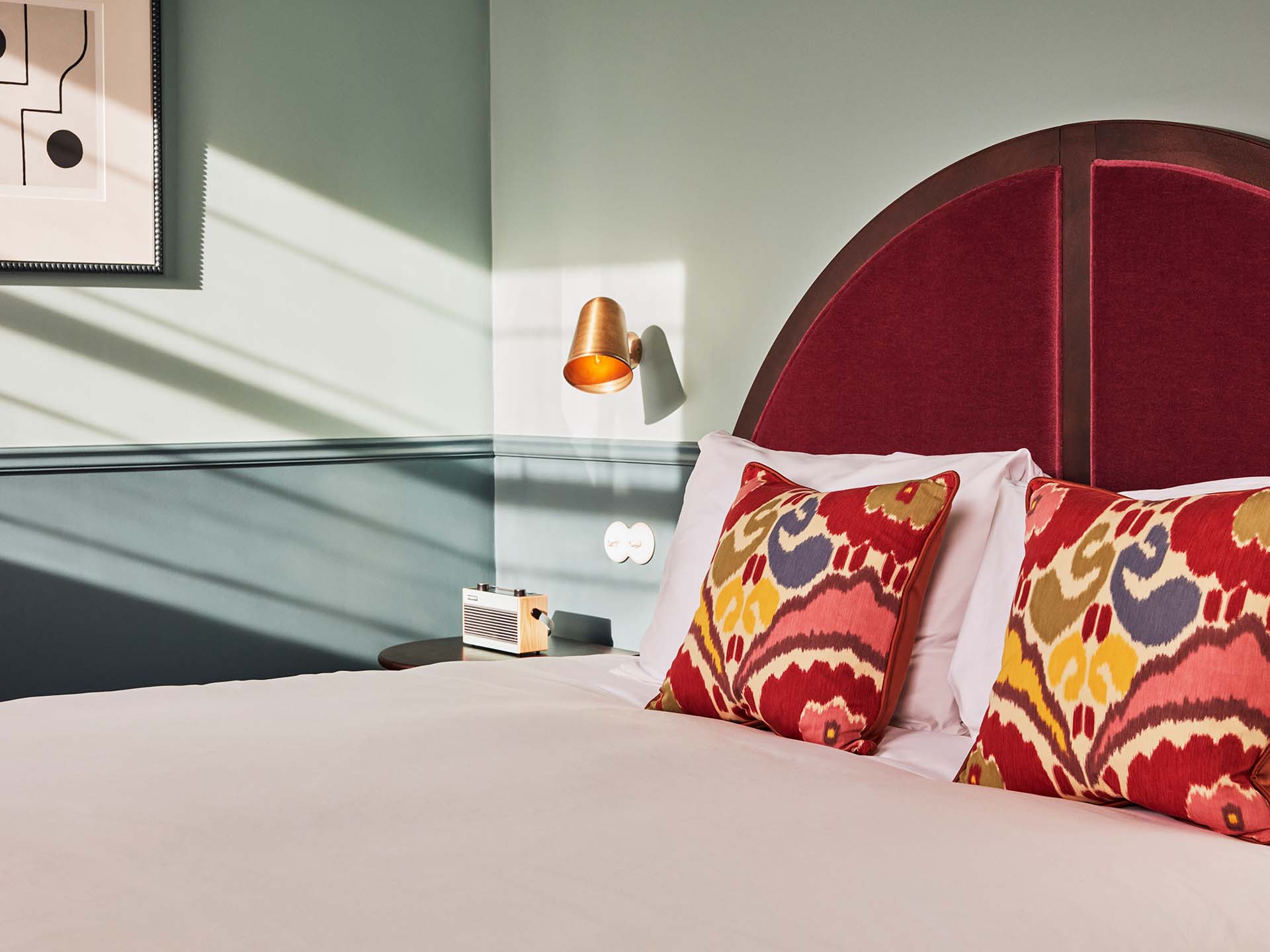 Arredamento di una camera d'albergo con testiera in velluto rosso e cuscino decorativo sul letto.