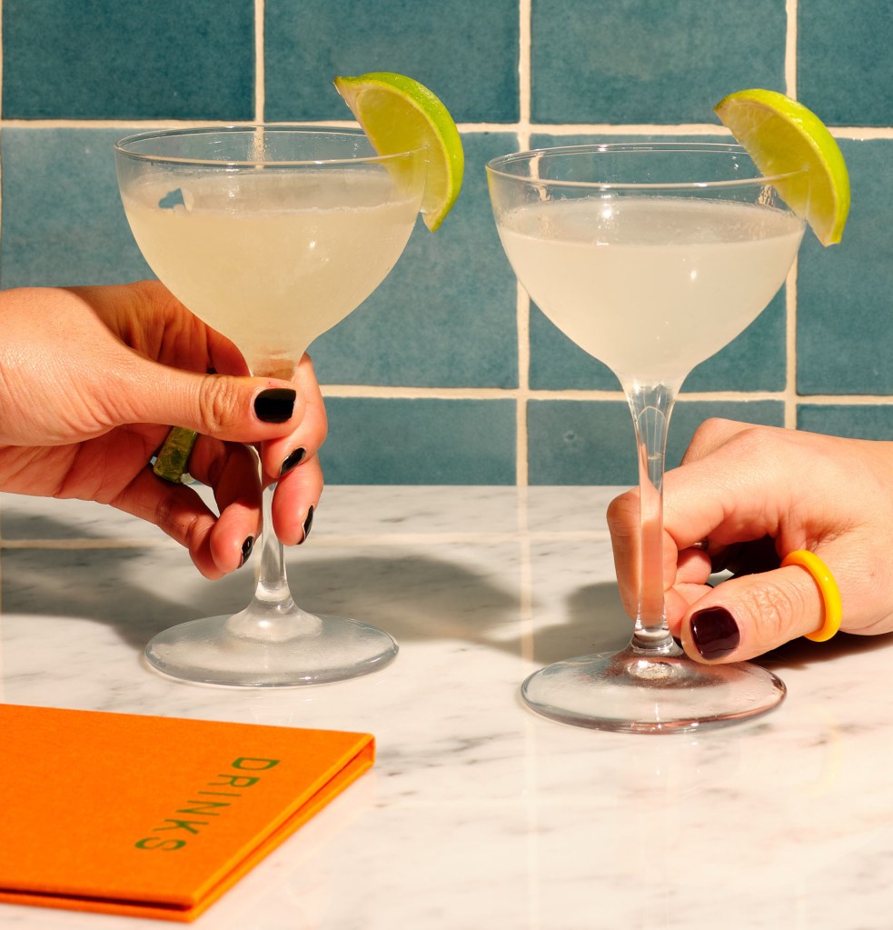 Two hands holding a Daiquiri Classico drink each with menu book on the side.
